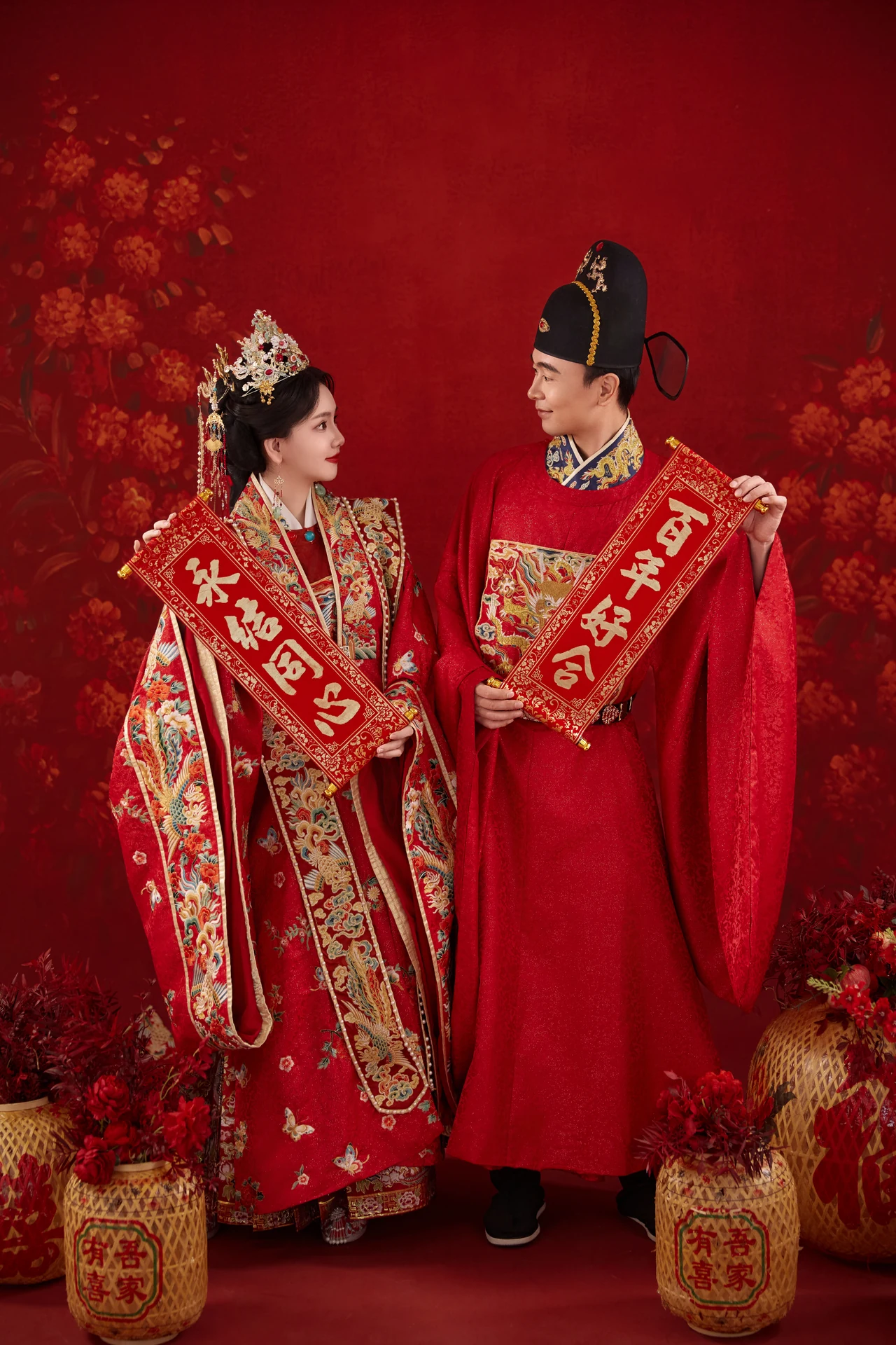 翟世雄与张欣怡身着红色中式礼服，手持喜庆卷轴相望的合照
